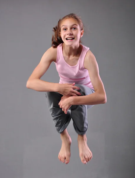 Healthy young happy smiling teenage girl skipping and dancing in studio. Child exercising with jumping on grey background.
