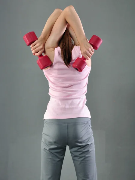 Teenage sportive girl is doing exercises to develop with dumbbells muscles on grey background. Sport healthy lifestyle concept. Sporty childhood. Teenager exercising with weights.