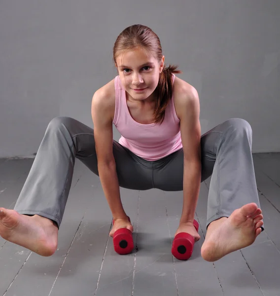 Teenager girl doing exercises with dumbbells to develop with dumbbells muscles on grey background. Full length portrait of teen child exercising with weights.