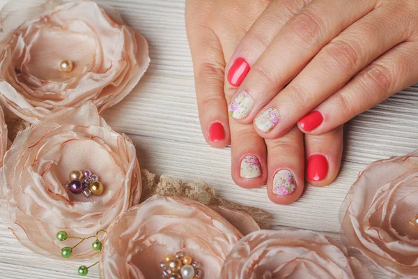 Red nail art with printed flowers on wooden background
