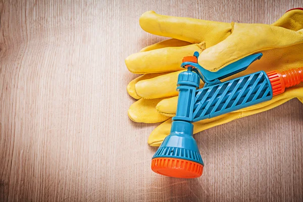 Safety gloves with garden water sprayer on wooden board gardenin