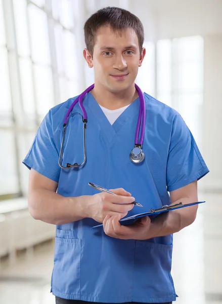 Young doctor holding clipboard and ballpoint pen looking at came