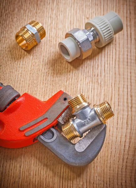 Pipe fixtures and monkey wrench on wooden board close up