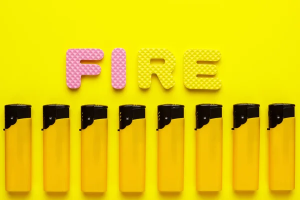 Plastic lighters and word fire on yellow background