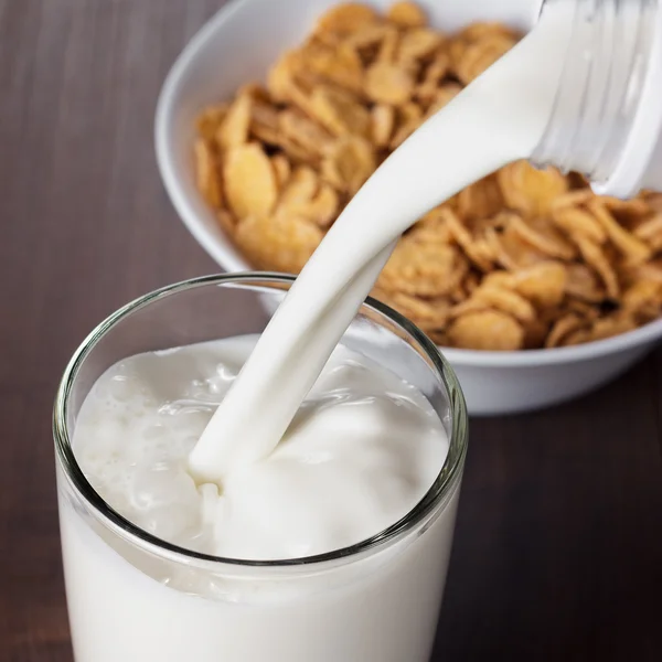 Milk pouring into glass and bowl with cornflakes