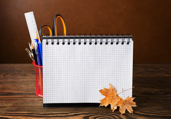 School equipment with pencils, notebook and dry autumn leaves  on wooden table .