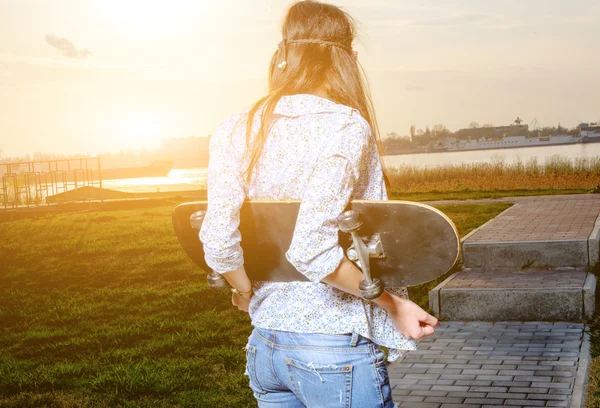 Skater young woman on sunset. Woman with skateboard in her hands outdoors looking at sunset, copyspace