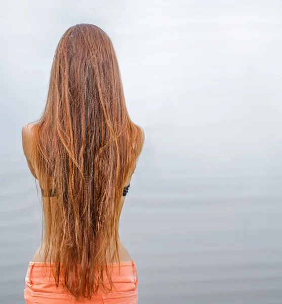 Rear view of long haired redhead woman posing against sea water, a lot of space for text