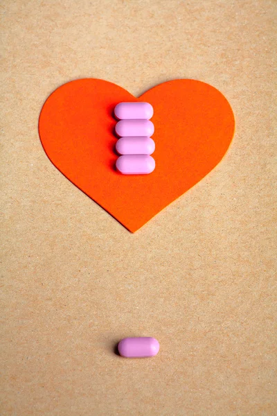 Red heart shape over craft paper with row of small pink pill on and copy space on the top. Heart health concept.