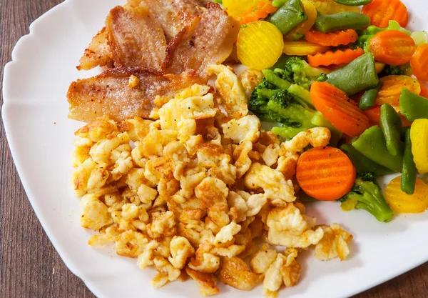 Scrambled eggs with bacon and vegetables mix in a plate on wooden table