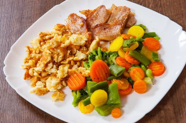 Scrambled eggs with bacon and vegetables mix in a plate on wooden table