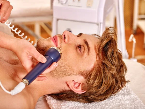 Young man receiving electric facial massage.