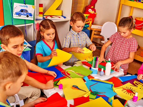 Kids holding colored paper on table in kindergarten .