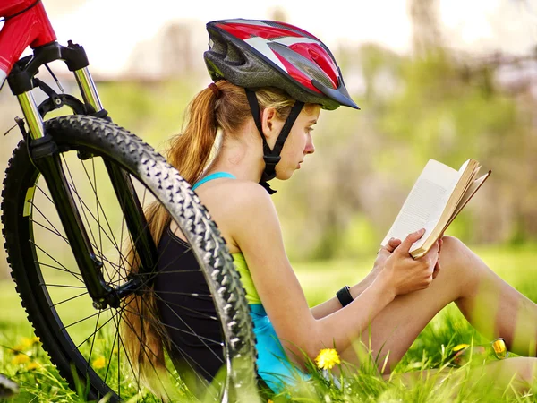 Bikes cycling girl wearing helmet read book on rest near bicycle.