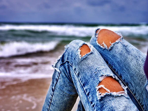 Legs of woman sitting on coast near ocean with waves. Hot dog leg selfie.