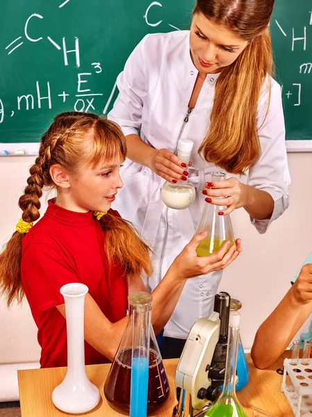Child girl and teacher holding flask in chemistry class.