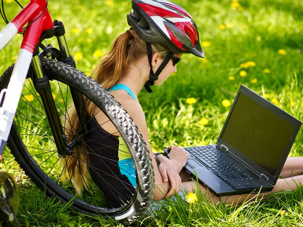 Bikes girl in cycling helmet sitting near bicycle with laptop.