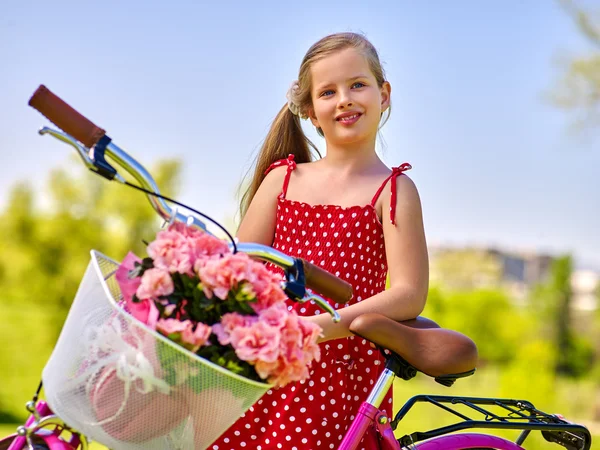 Child girl wearing red sundress rides bicycle into park.