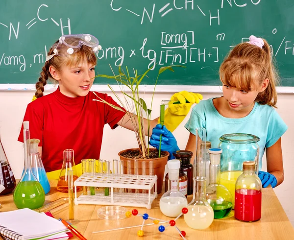Children holding flask and plant in biology class.