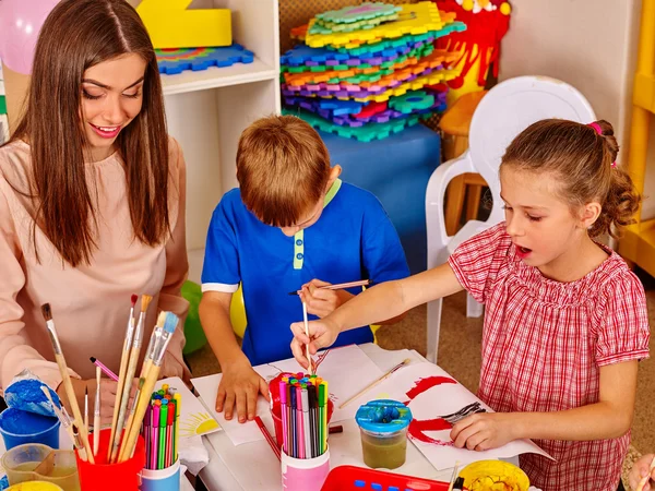 Children with teacher woman painting on paper in kindergarten .