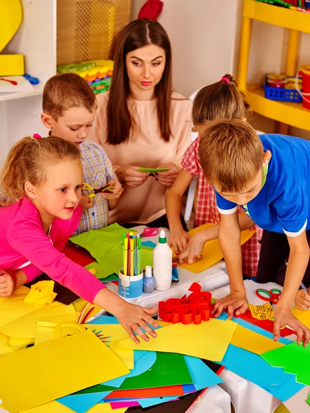 Children with teacher are making something out of colored paper.