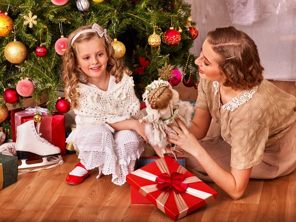 Kid with mother receiving gifts under Christmas tree.