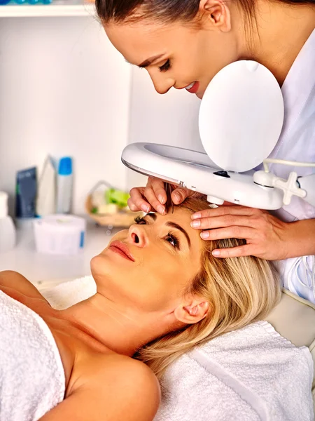 Woman middle-aged in spa salon with cosmetic lamp .