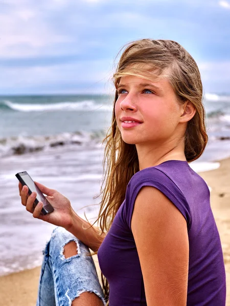 Girl with mobile phone sitting on sand near sea.