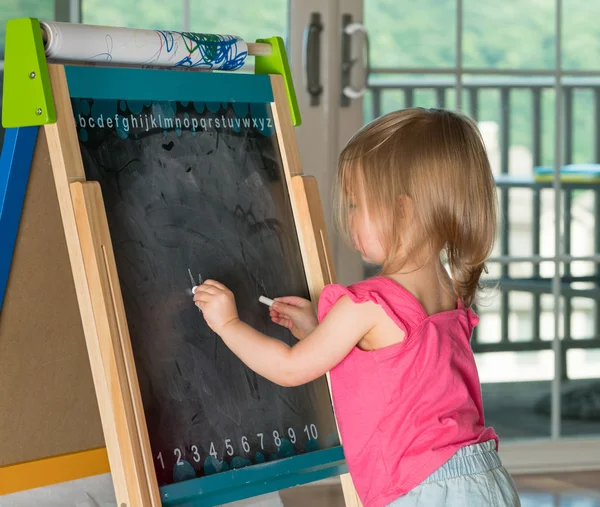 Young baby girl drawing at blackboard