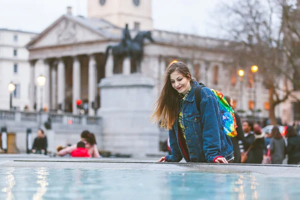 Young woman looking at herself into a fountain in London