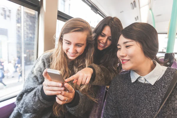 Three women looking a smart phone on the bus