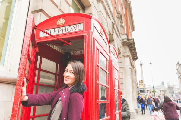 Young woman in London in front of a typical red phone booth