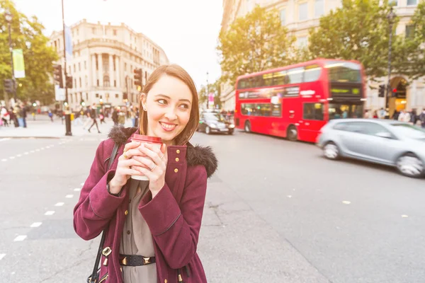 Woman in London standing by a busy road holding coffee