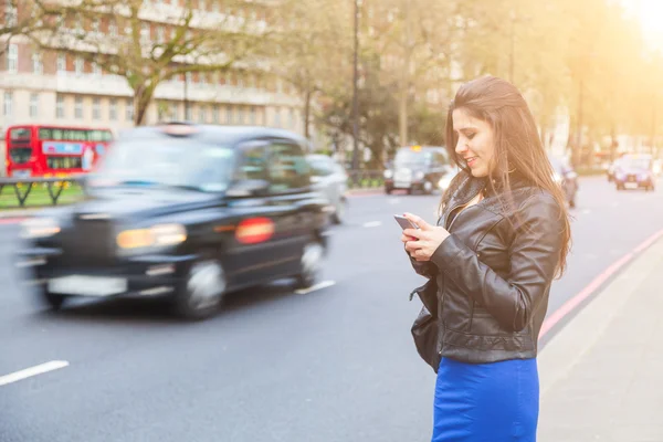 Young woman typing on her smart phone by a busy road in London