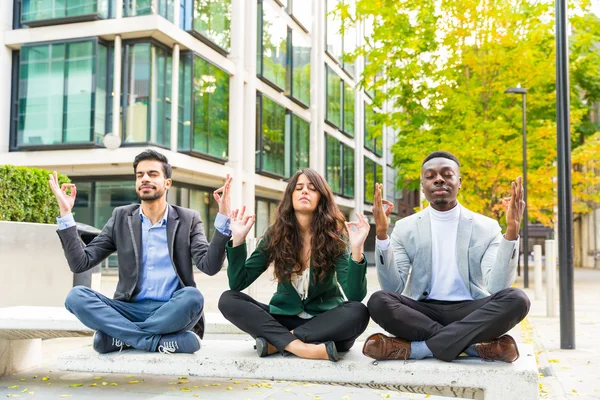 Three young business people doing yoga excercises during a break