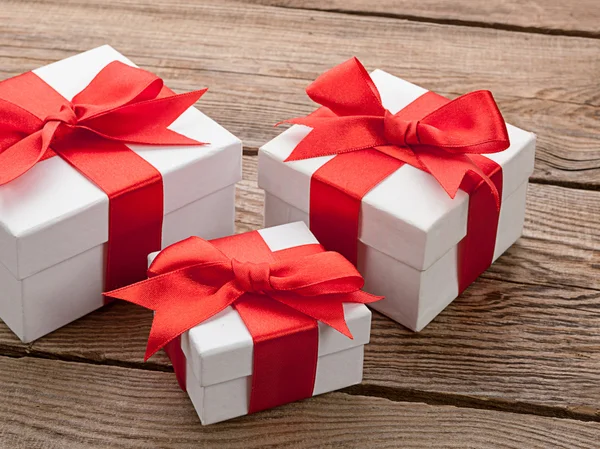 White gift box with red ribbon on old board.