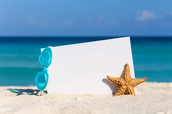 Blank white board, swimming glasses and starfish on sand against