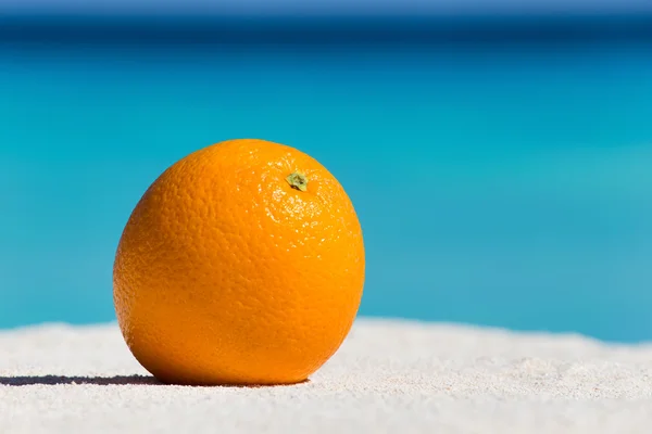 Orange fruit on sand against turquoise caribbean sea water