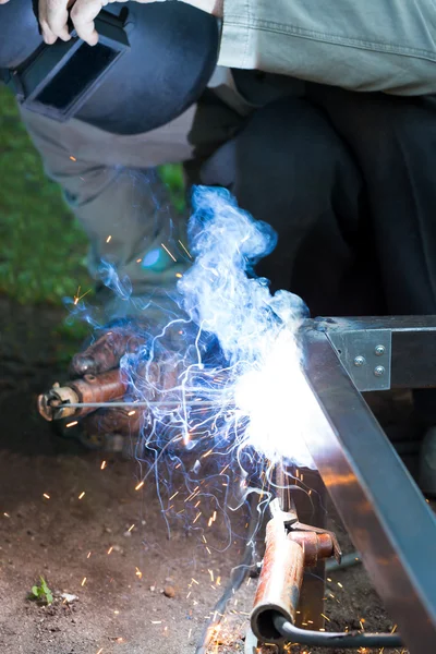 Worker in protective mask welding steel railings outdoors