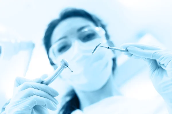 Dentist in mask holding angled mirror and drill