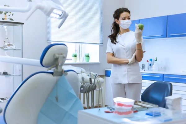 Dentist in mask holding green apple.