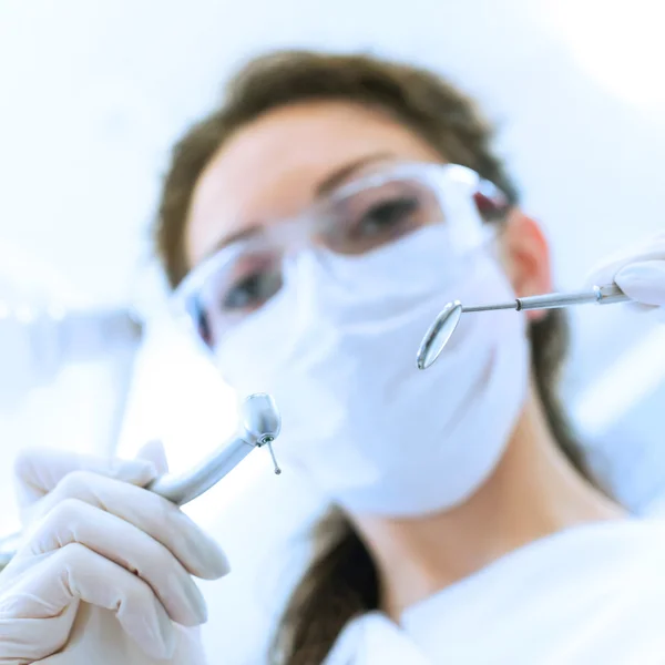 Dentist in mask holding angled mirror and drill