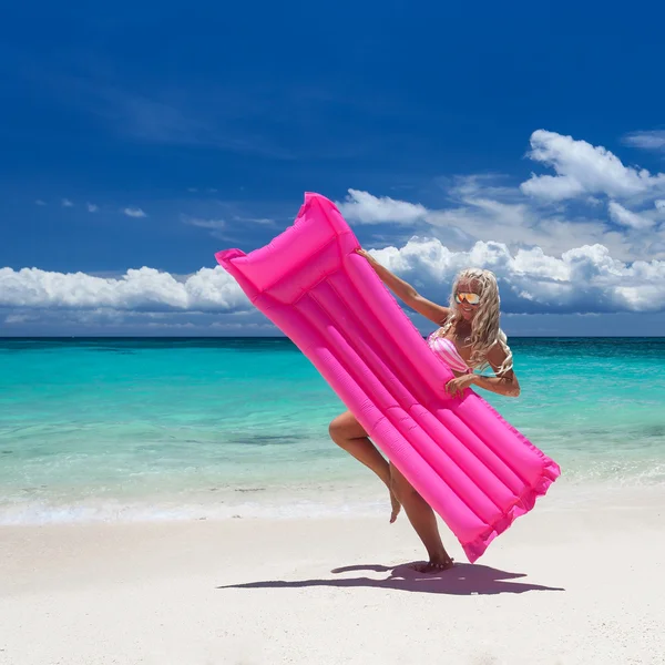 Woman with pink swimming mattress on tropical beach