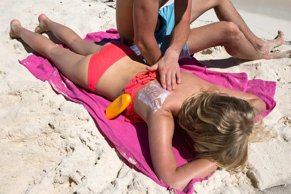 Man applying SPF sign with sun protection lotion on a woman back