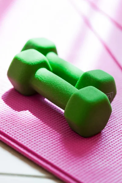 Two green dumbbells on pink yoga mat