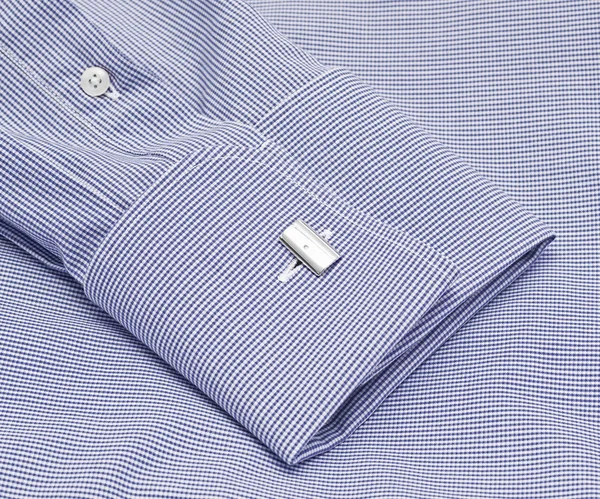 The blue sleeve of a plaid shirt with a cuff link