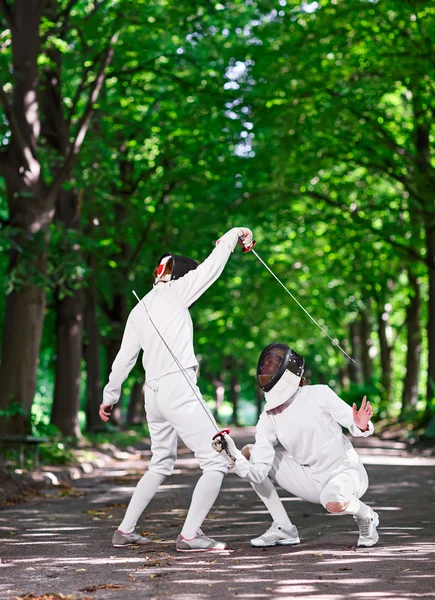 Two rapier fencers women fencing on park path