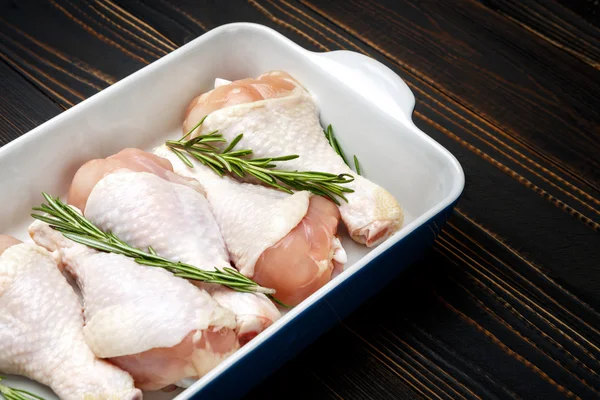 Raw chicken legs in baking dish on a wooden background