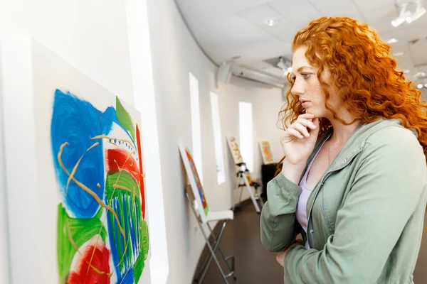 Young caucasian woman standing in art gallery front of  paintings