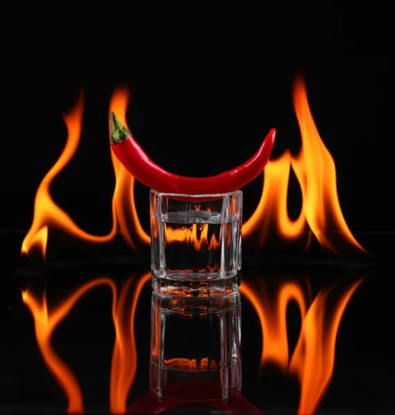Hot chili pepper in a shot  glass with a fire on a black background